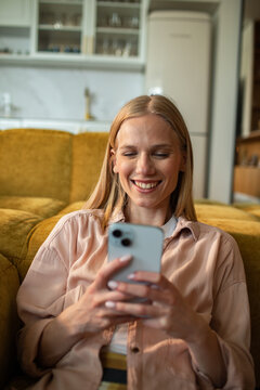 Smiling woman using smartphone on yellow sofa in modern living room