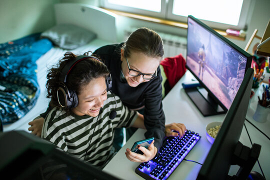 Two friends playing pc game and sharing smartphone at home
