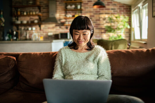 Smiling woman using laptop on sofa at home