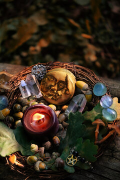 burning candle, moon amulet, crystals, acorns, oak leaves on tree trunk outdoor, dark natural abstract background. practical magic, witchcraft, spiritual esoteric wiccan ritual, druids practice