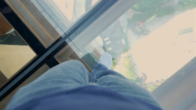 First person view walking across a transparent glass floor on a high rise observation deck, revealing the city far below and creating a thrilling height experience.
