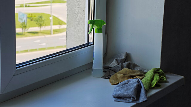 Cleaning spray and microfiber cloths resting on a window sill, ready for domestic work, with an outside urban landscape