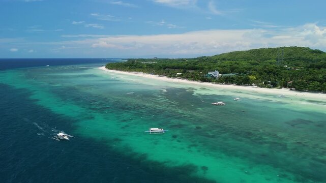 Drone follows a longboat arriving near Dumaluan Beach, revealing turquoise reef flats, white sand, boats, and the Panglao coastline in Bohol