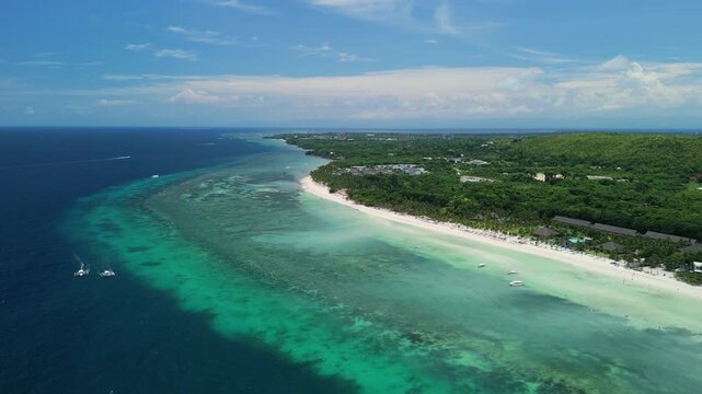 Aerial drone pulls back over Dumaluan Beach, showing white sand coastline, reef flats, turquoise water, boats, and the green inland hills of Panglao, Bohol