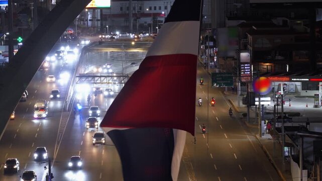 Large Dominican Republic flag waving in wind with traffic and city lights in background at night in Santo Domingo