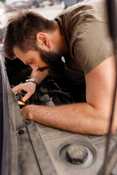 Vertical orientation bearded man mechanic repairing broken car engine under open hood on street auto service inspection close up driver fixing vehicle motor breakdown vehicle troubleshooting maintenan