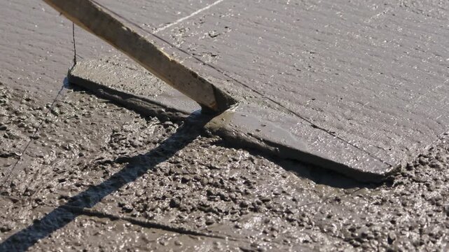 Screeding fresh concrete surface during foundation slab construction close up