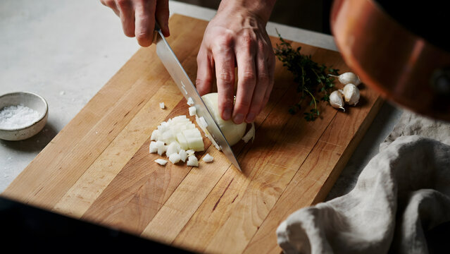 A chef chopping fresh onion on a wooden cutting board in a professional kitchen
