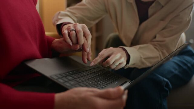 Middle aged Caucasian woman helping senior mother use laptop, guiding her hand on keyboard. Footage is suitable for senior care services, digital literacy, or family support concepts