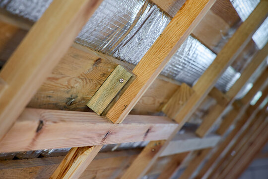 Wooden roof framing with installed silver radiant barrier foil insulation attached to timber rafters inside residential building attic under construction.