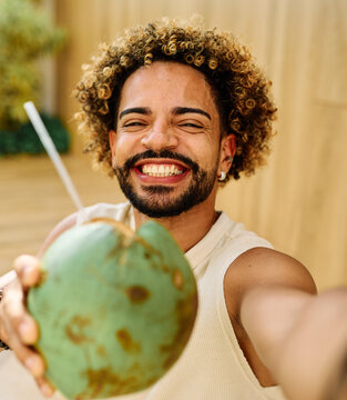 Young man enjoy coconuts while sitting in water at a pool area and using a smartphone camera  taking a selfie photo in a warm location during summer