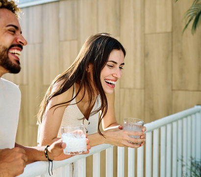 Two people enjoy cocktail drink or alcohol and juice while sitting in water at a pool area in a warm location during summer