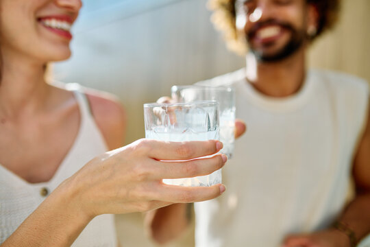 Two people enjoy cocktail drink or alcohol and juice while sitting in water at a pool area in a warm location during summer