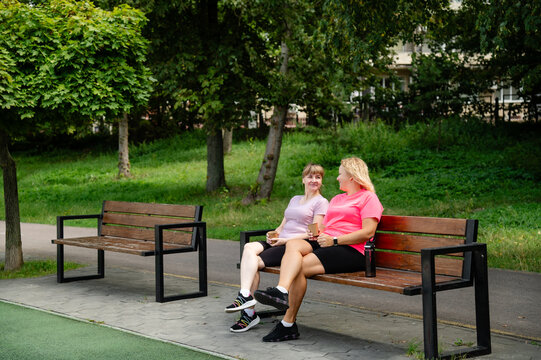 Two women share a conversation while sitting on benches in a park on a sunny day