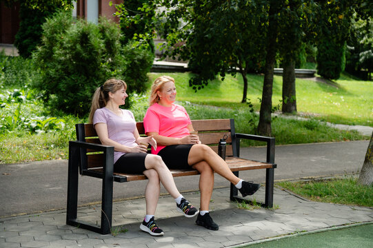 Two women sitting on a bench at a park after exercising