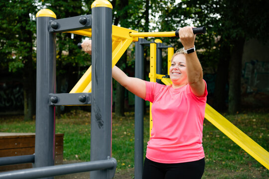 Woman exercises on outdoor fitness equipment in a park during daytime