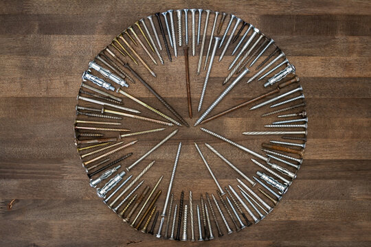 Circle made of various screws and nails on brown wood texture. Industrial flat lay. Carpentry still life.