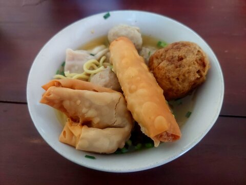 A bowl of Indonesian bakso soup with noodles, wonton, fried snacks, and chopped scallions.
