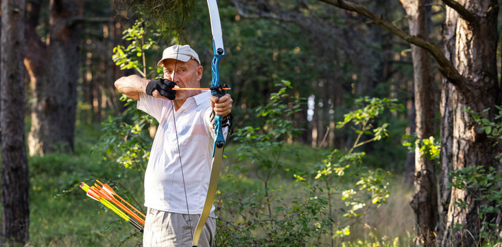 Senior man practicing recurve archery in forest during outdoor training