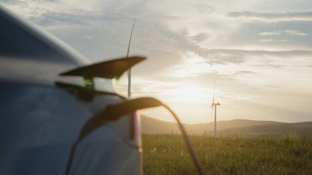 Electric car charges with cable connected near wind turbines at sunset. The scene reflects renewable energy, clean electricity, and sustainable technology driving modern mobility and environmental .