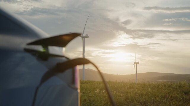 Electric car charges at wind farm during sunset. The moment symbolizes renewable energy, clean electricity, and sustainable technology driving modern industry and future mobility.