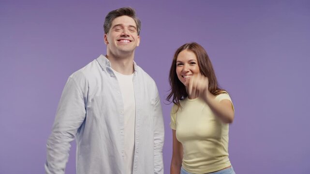 Happy young couple - man and woman waving to camera with cheerful expressions. Friendly greeting, saying goodbye, warm welcome, positive emotions and everyday communication.