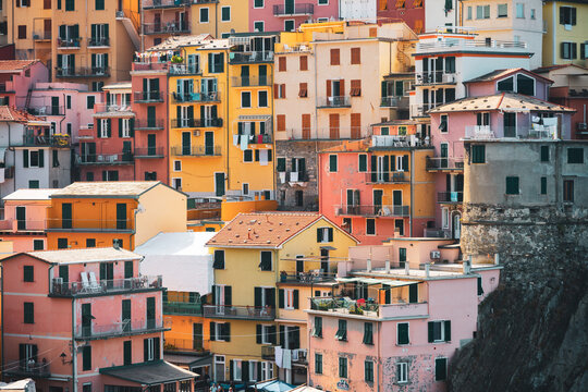 Manarola village in Cinque Terre has colorful houses stacked on the hillside. Balconies overlook the sea. It is midday and the houses show their cheerful colors under the sun.