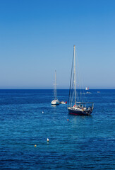 Fototapeta premium Sailboats Moored on Calm Deep Blue Sea Under Clear Sky with Distant Boats on Horizon Peaceful Summer Sailing Seascape Nature View
