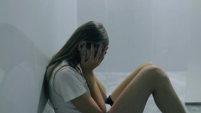 Sad generation z teenager sitting by wall hiding face in hands.