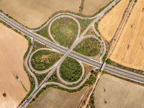 Aerial view of a symmetrical cloverleaf highway interchange. Cars on the road network show transportation and logistics in a rural landscape, symbolizing connectivity and infrastructure.