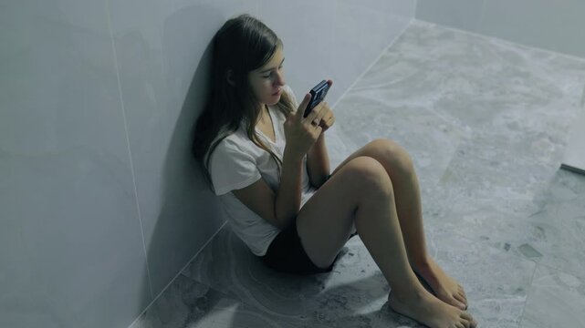 Sad generation z teenager using smartphone sitting floor.