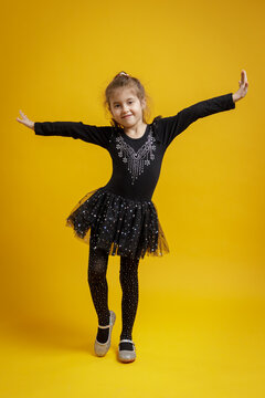 Smiling little girl in black dance costume posing on yellow background. Child portrait for dance, fashion and education.
