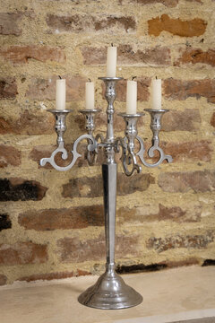 Elegant silver candelabra with five white candles against a rustic brick wall. Classic vintage candlestick for romantic dinners, event decoration, and timeless home interior design.