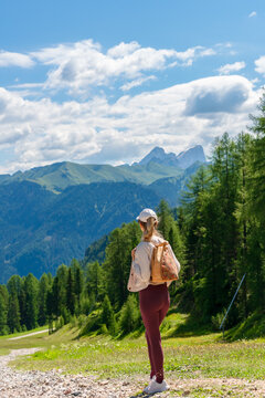 Female traveler standing on a mountain path while overlooking a breathtaking alpine panorama beneath dramatic clouds. A scenic image illustrating exploration, outdoor adventure, travel inspiration