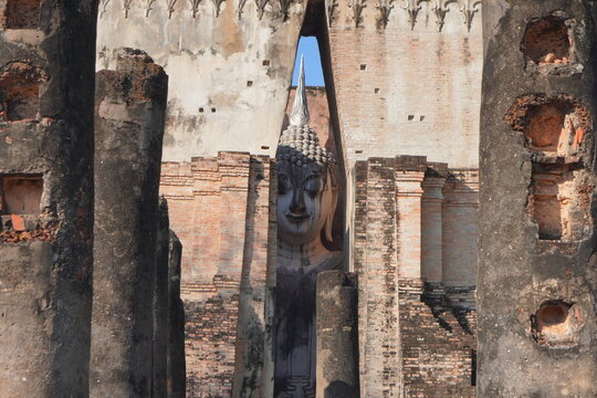 Ancient Phra Achana Buddha statue seen through the narrow opening of the mandapa at Wat Si Chum, Sukhothai Historical Park, Thailand.