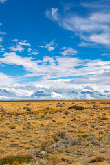 Obraz premium Wide-angle vertical shot capturing the endless horizon of the Patagonian pampas, with a simple wire fence line, leading the eye to a majestic, cloud-shrouded mountain range 