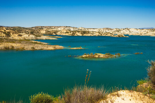 Serene turquoise water of embalse de la pedrera reservoir reflecting clear blue skies, surrounded by arid badlands terrain and rugged eroded landforms in costa blanca, spain