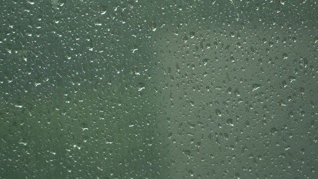 Raindrops Cascading Down a Windowpane During a Gloomy Day with Green Blurred Background
