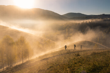 Golden morning light and drifting mist surround hikers on rolling countryside hills during autumn. © Andrei Tomas