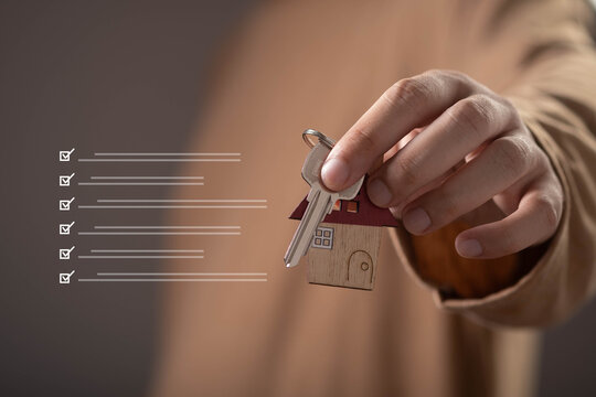 Hand holding house keys with home-shaped keychain and property checklist, representing real estate purchase, homeownership, property investment, mortgage approval, relocation, and housing solutions.