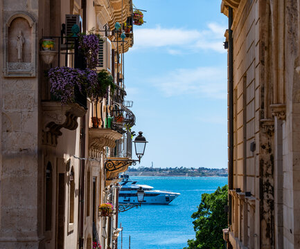 a glimpse of the blue Sicilian sea with a motorboat passing by, seen from the top of a narrow alley flanked by houses