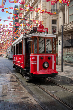 Istanbul, turkey, august 2, 2025 red and white nostalgic tram driving on cobblestone street in beyoglu, istanbul, decorating with flags and people walking