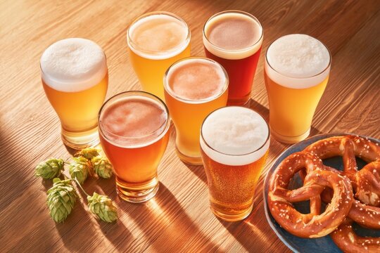 Overhead flat lay of craft beer glasses with pretzels and hops on wooden table