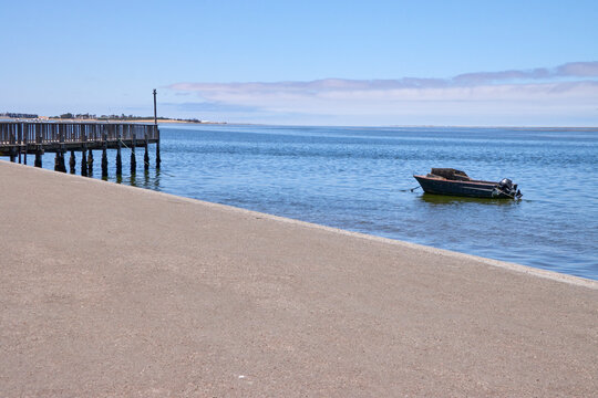 Ein Steg und ein kleines Boot liegen am Wasser in Walvis Bay in der Region Erongo, Namibia.