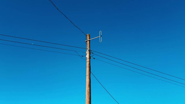 Old wooden antenna on pole against clear blue sky, weathered wood post with thin wires stretching across frame, rooftop edge