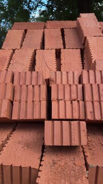Stack of red clay building bricks outdoors, perforated construction materials piled up for masonry work, textured terracotta blocks with trees in background