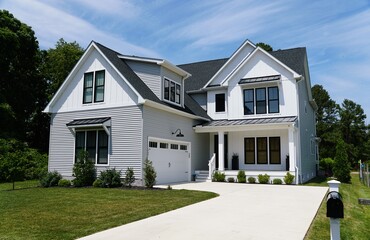 Fototapeta premium A two-story modern suburban home with white siding, black trim, gabled roofs, landscaped yard, and paved driveway leading to double garage near Rehoboth Beach, Delaware, U.S.A 