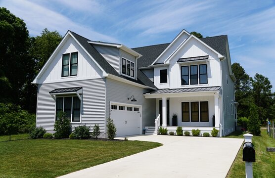 A two-story modern suburban home with white siding, black trim, gabled roofs, landscaped yard, and paved driveway leading to double garage near Rehoboth Beach, Delaware, U.S.A 