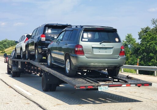 Pennsylvania, U.S.A - Jul 19, 2026 - A flatbed trailer carrying three SUVs, including green Toyota Highlander, traveling on the highway