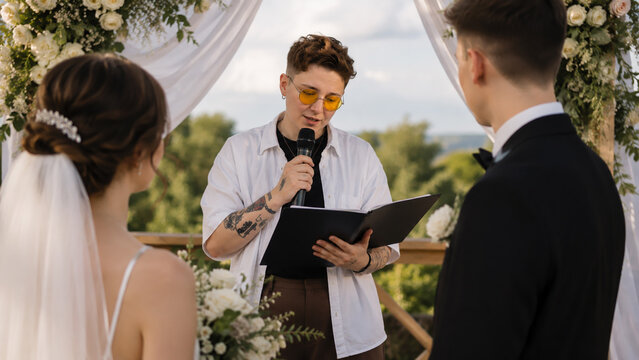 Wedding officiant conducting an outdoor wedding ceremony while reading vows to the bride and groom. Marriage celebration, romance, love, commitment and event planning concept.